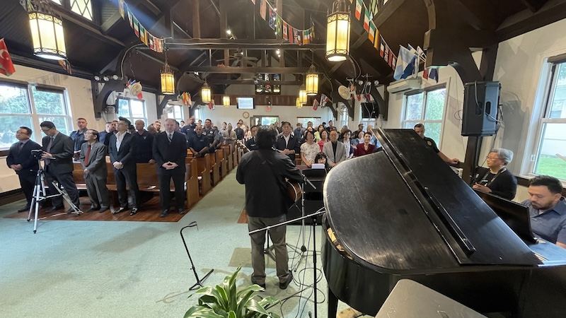 Congregation standing in the sanctuary during worship, flags of many nations overhead